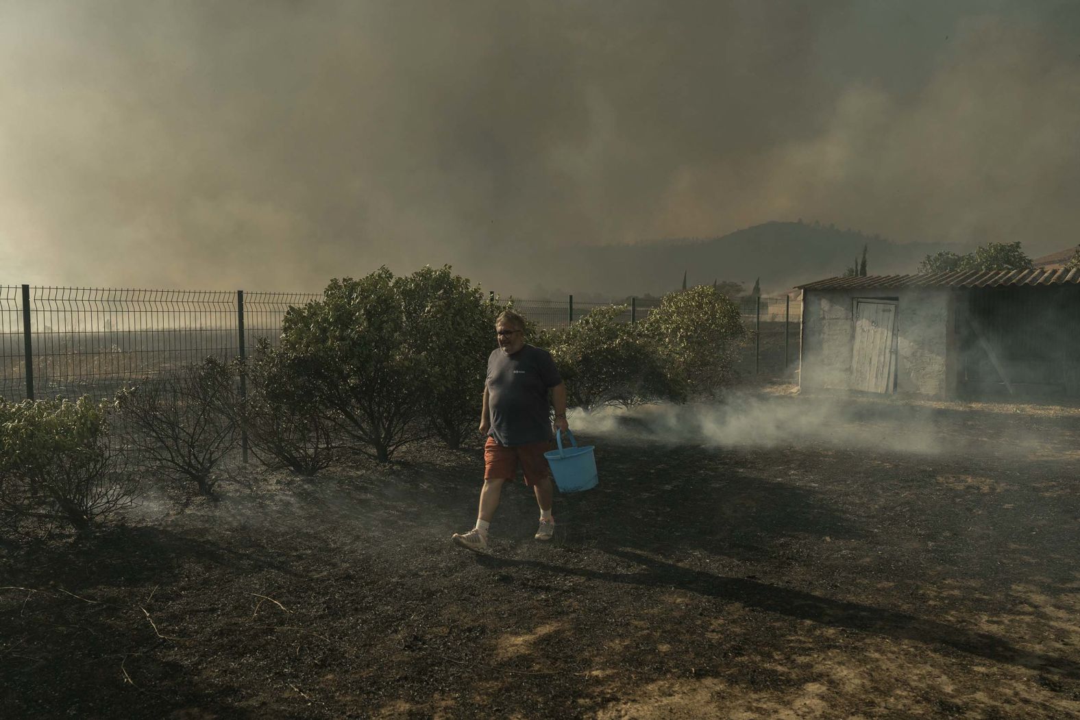 A resident carries a water bucket to extinguish a wildfire in Tournissan, France, on Tuesday, August 5.