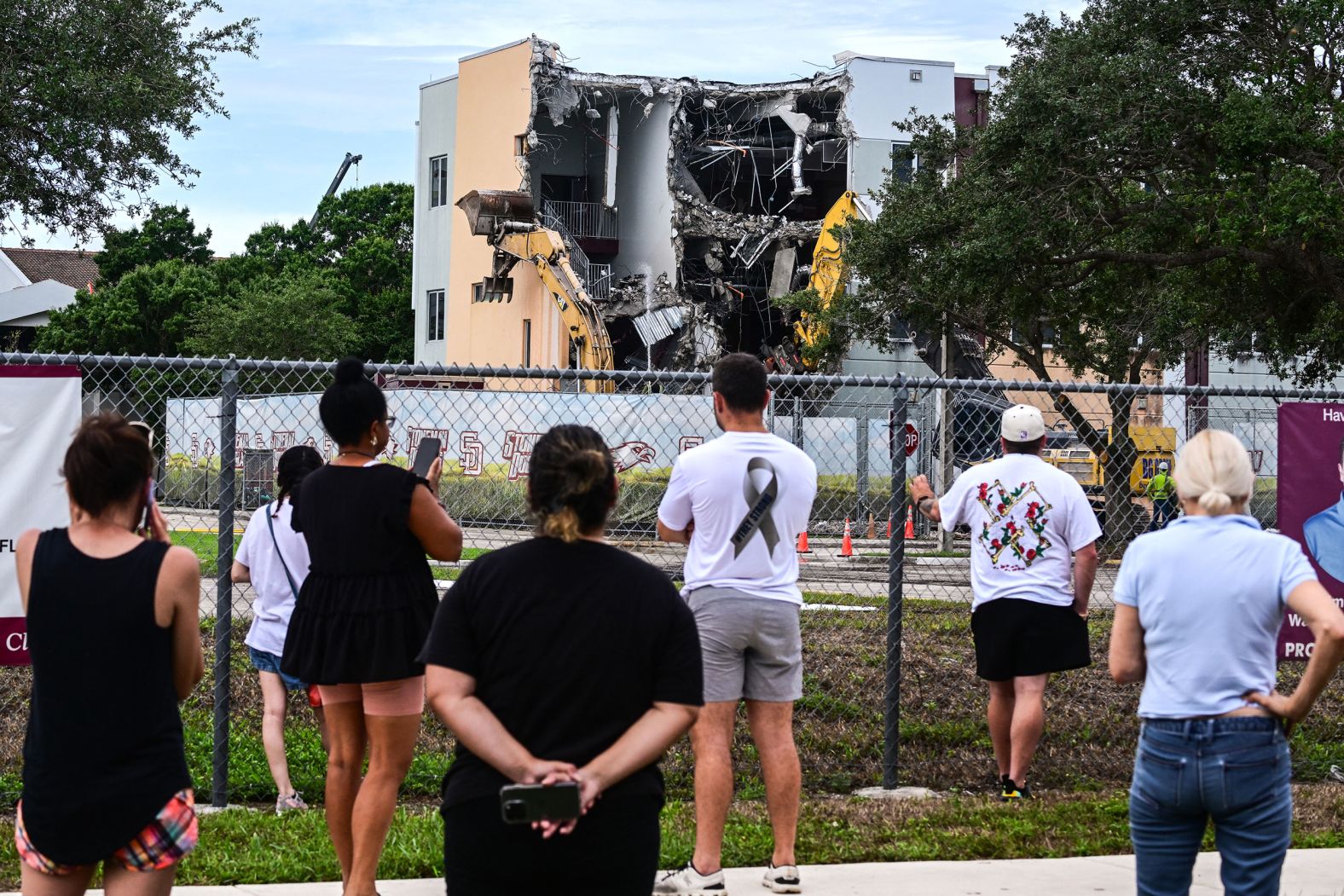 People watch on Friday, June 14, as crews begin to <a href="index.php?page=&url=https%3A%2F%2Fwww.cnn.com%2F2024%2F06%2F14%2Fus%2Fparkland-demolish-stoneman-douglas-high-school-shooting%2Findex.html">demolish the building</a> where 17 people were killed during the 2018 mass shooting at Marjory Stoneman Douglas High School in Parkland, Florida.