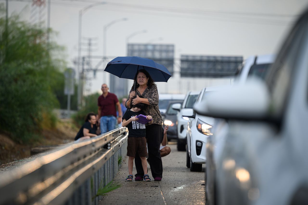 A woman looks for further incoming rockets as she shelters by the side of the motorway with a young boy on October 16, in Tel Aviv, Israel.