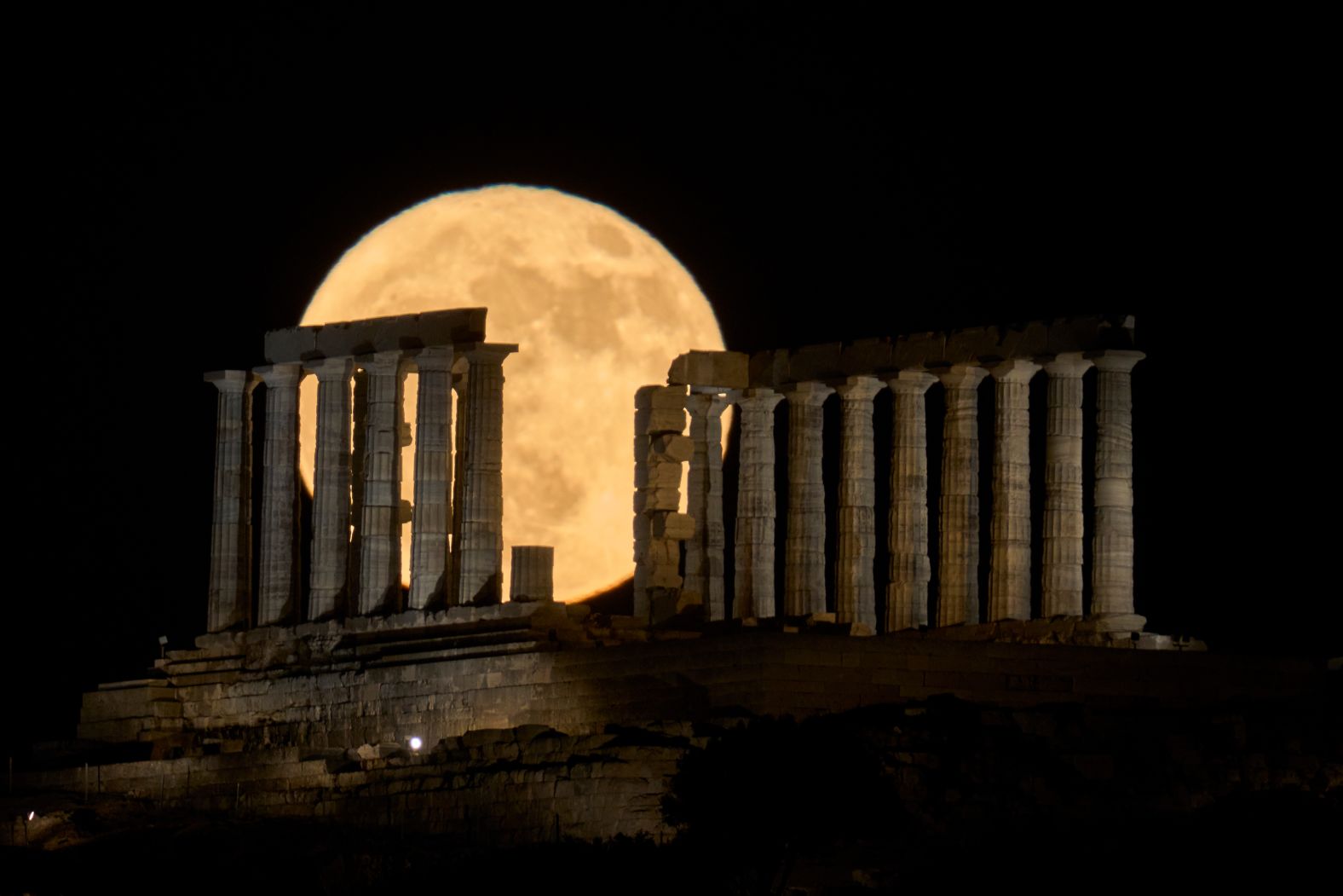 A full moon is seen behind the Temple of Poseidon in Cape Sounion, Greece, on Wednesday, June 11.