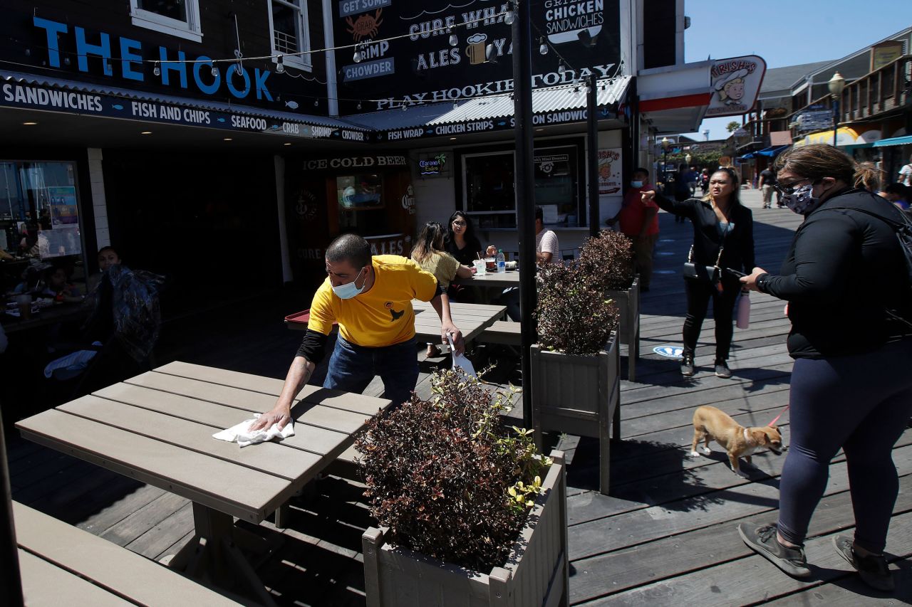 A man wears a face mask while cleaning an outdoor dining table at The Hook at San Francisco's Pier 39 on June 18.