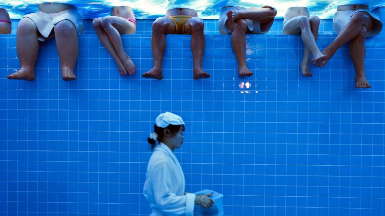 A waitress wearing bathrobe walks by mannequins at a restaurant setup as a bathing center at an old Beijing's hutong alley inside a shopping mall in Beijing, Sunday, Aug. 11, 2024. (AP Photo/Andy Wong)