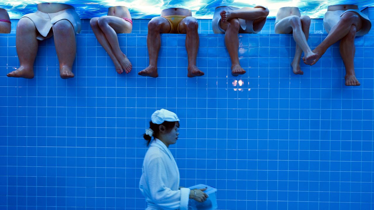 A waitress wearing bathrobe walks by mannequins at a restaurant setup as a bathing center at an old Beijing's hutong alley inside a shopping mall in Beijing, Sunday, Aug. 11, 2024. (AP Photo/Andy Wong)