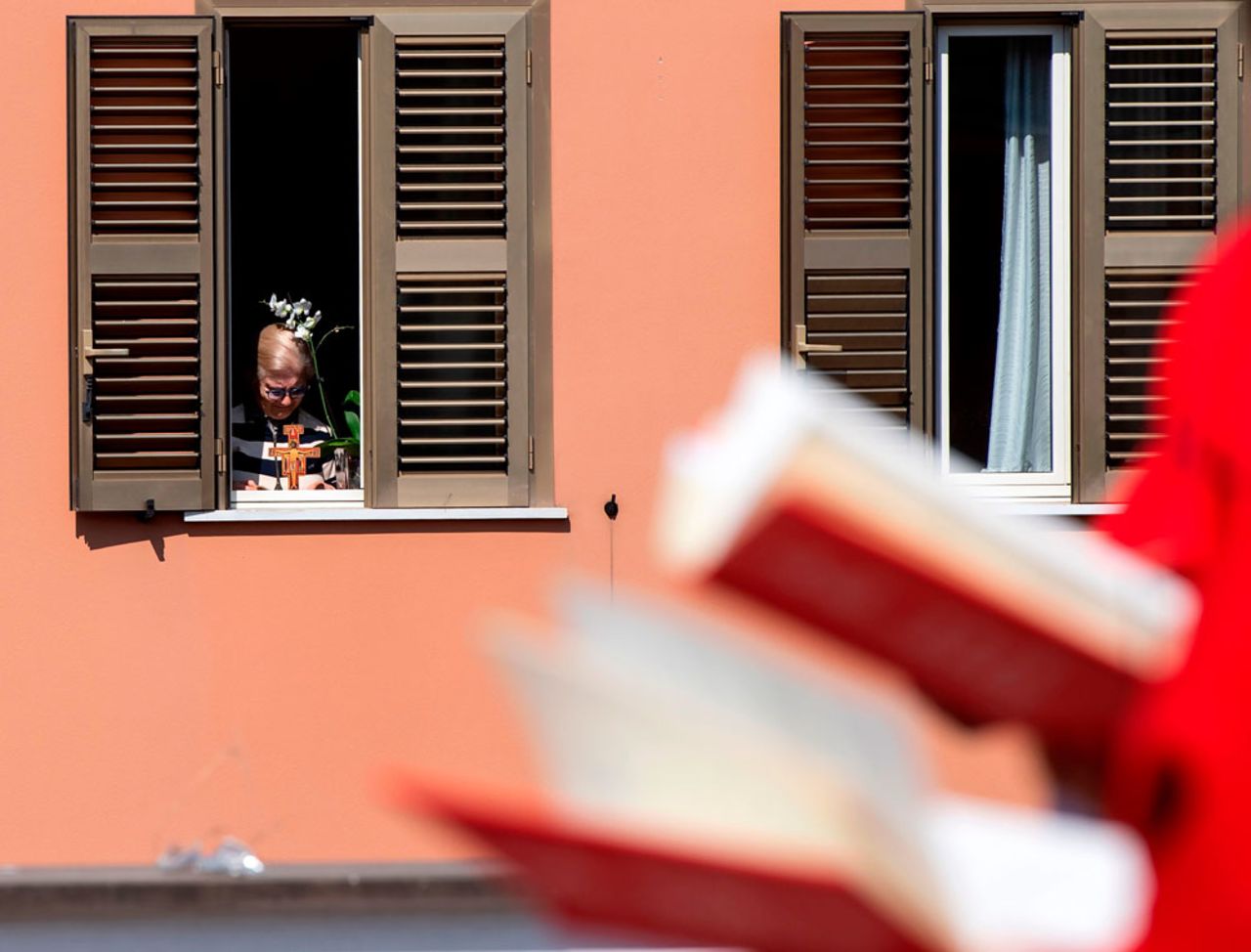 A resident watches from her apartment as Palm Sunday mass is celebrated on the rooftop of the San Gabriele dell'Addolorata church in Rome on April 5, during the country's lockdown.