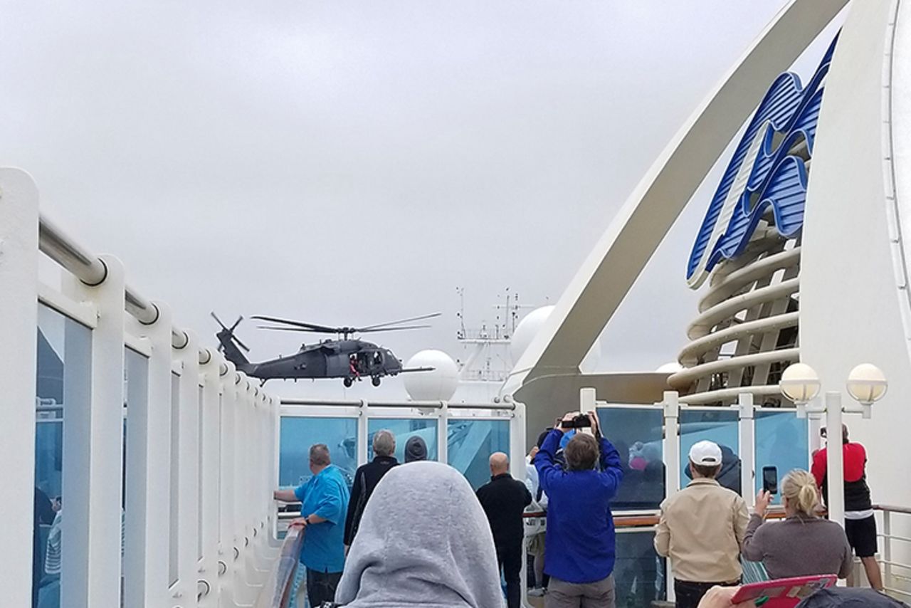 In this photo provided by Michele Smith, passengers look on as a Coast Guard helicopter hovers above the Grand Princess cruise ship on Thursday, March 5, off the California coast.?