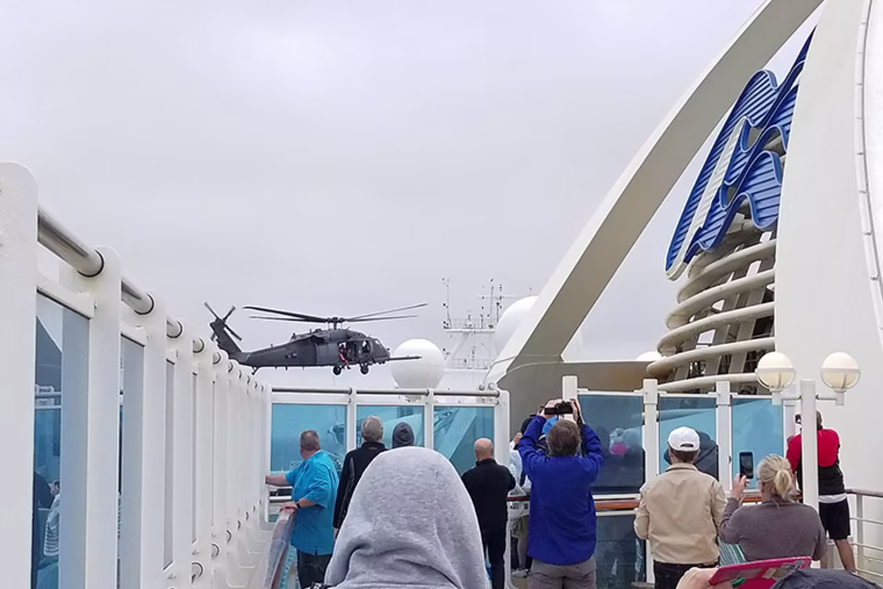 In this photo provided by Michele Smith, passengers look on as a Coast Guard helicopter hovers above the Grand Princess cruise ship on Thursday, March 5, off the California coast. 