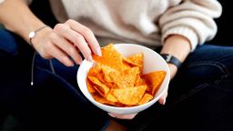 2BB48TH A close up of a caucasian female hands holding a white bowl containing  tangy cheese Doritos