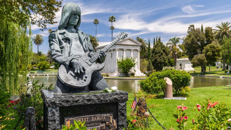 2BH0HT3 Close up Johnny Ramone bronze tombstone in Hollywood Forever, portraying him playing a guitar, with vegetation in the background