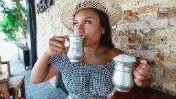 2J9KMCJ young indonesian girl drinking ayran in a silver cup wearing a hat during summer