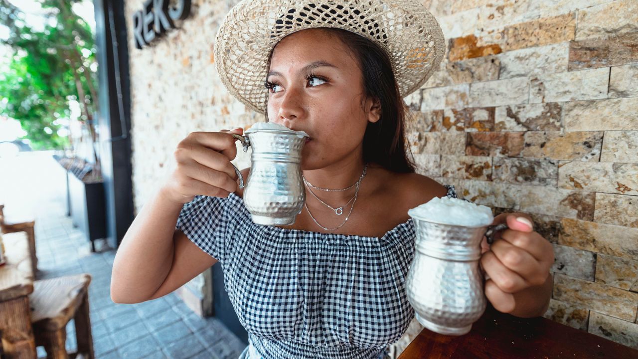 2J9KMCJ young indonesian girl drinking ayran in a silver cup wearing a hat during summer
