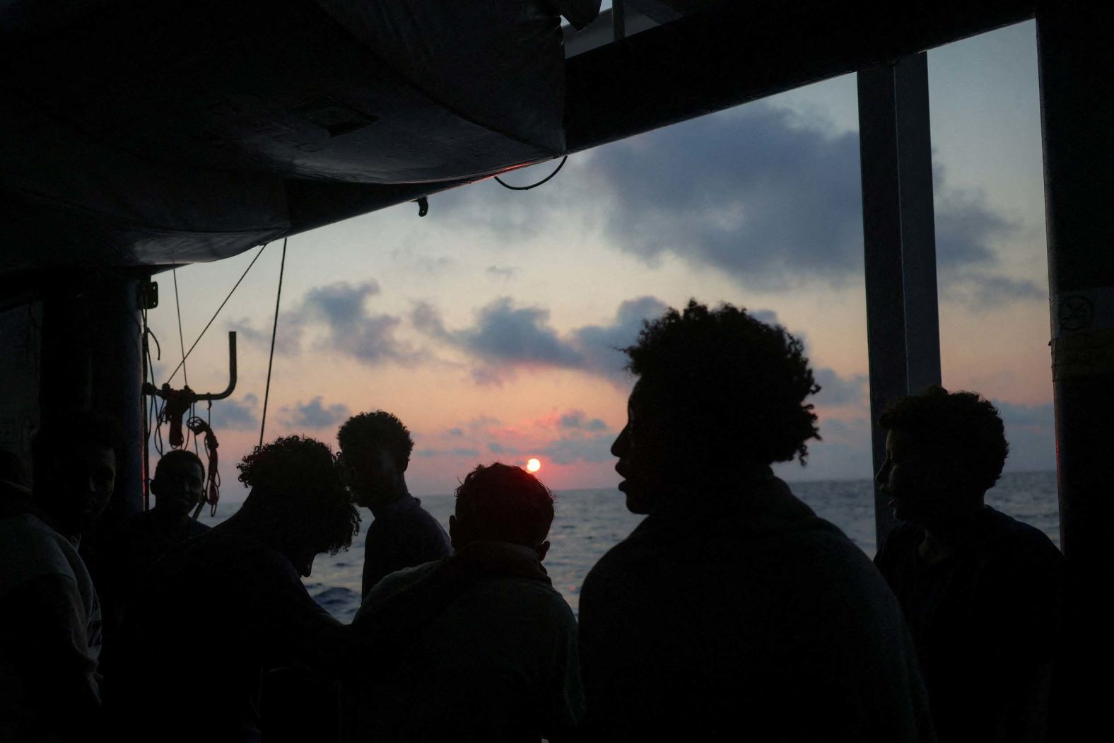 Rescued migrants look at a sunset aboard a migrant search-and-rescue ship operated by German NGO Sea-Watch as the ship makes its way toward Salerno, Italy, on Tuesday, August 12.