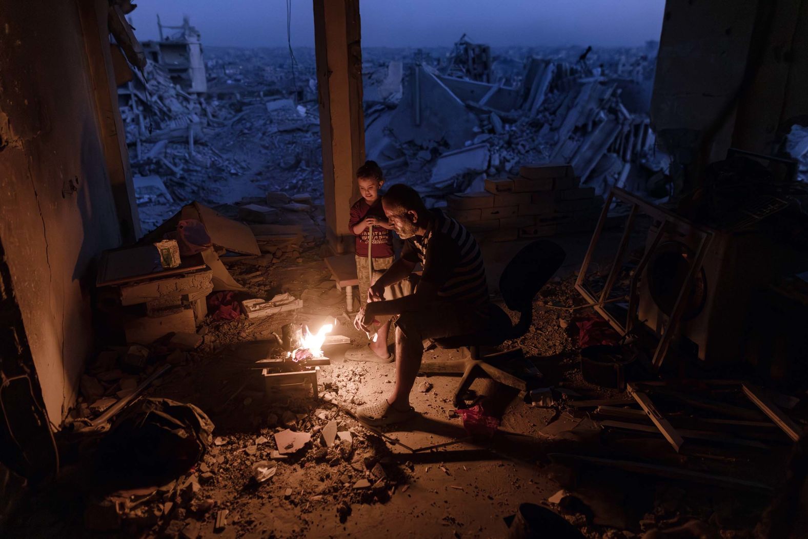 A man and boy sit by a fire at a destroyed home in Khan Younis, Gaza, on Sunday, November 2. Two years of Israeli bombardment <a href="index.php?page=&url=https%3A%2F%2Fwww.cnn.com%2F2025%2F10%2F19%2Fmiddleeast%2Fgaza-ceasefire-palestnians-ruins-reconstruction-latam-intl">has rendered much of the territory unrecognizable</a>.
