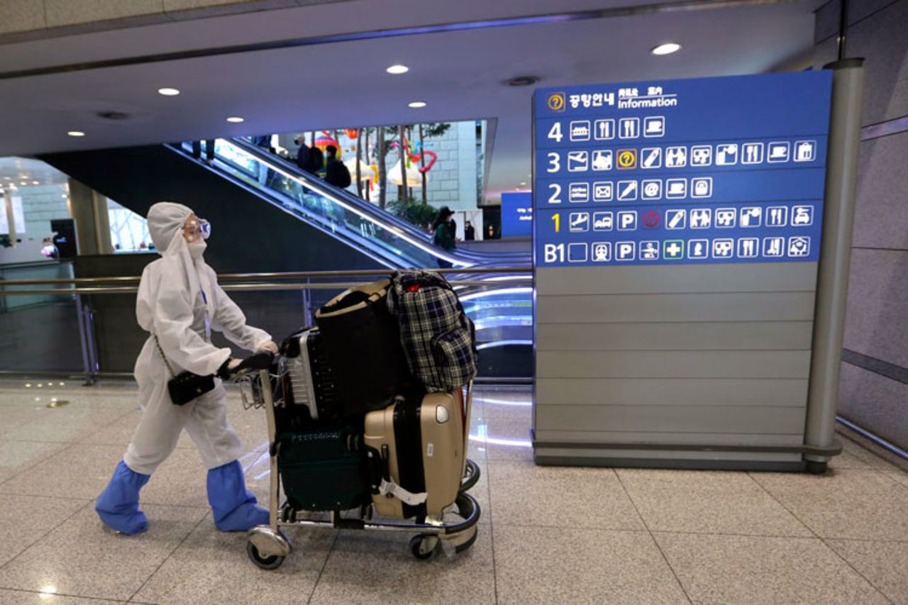 A woman wearing protective gear moves luggage as she waits for her flight at the Incheon Airport in Incheon, South Korea, on Thursday, March 19. 