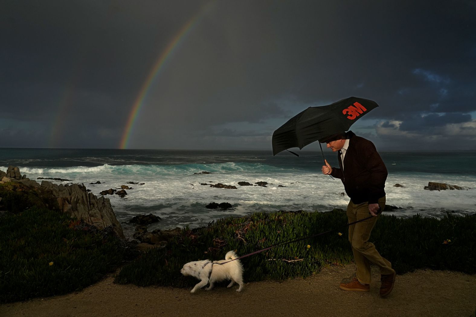 A man huddles under an umbrella as he walks a dog along the shoreline in Pacific Grove, California, on Friday, February 2. <a href="index.php?page=&url=https%3A%2F%2Fwww.cnn.com%2F2024%2F02%2F01%2Fworld%2Fgallery%2Fphotos-this-week-january-25-february-1-ctrp%2Findex.html">See last week in 31 photos</a>.