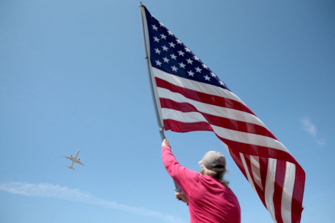 Dan Ray waves an American flag as a plane carrying former President Donald Trump takes off from the Palm Beach International Airport in Florida on Monday, April 3. Trump was heading to New York for an expected arraignment on Tuesday. 
