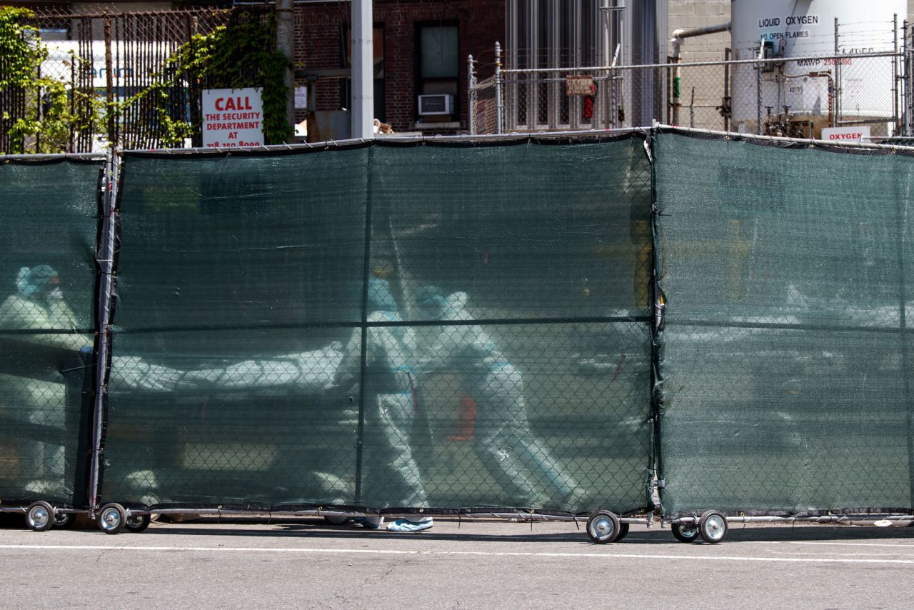 Hospital personnel behind a barricade move deceased individuals to the overflow morgue trailer outside The Brooklyn Hospital Center on May 7, in the Brooklyn borough of New York City. 