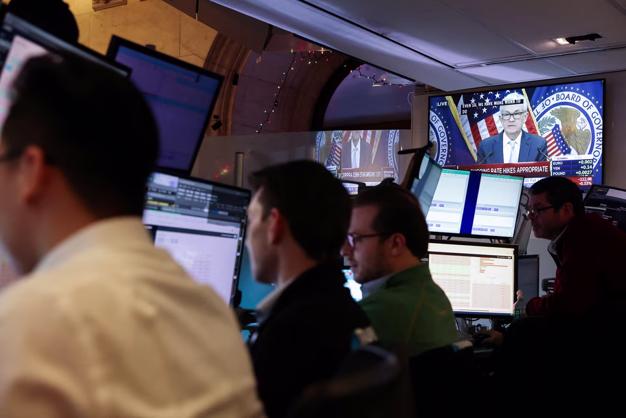 Traders are seen working at the New York Stock Exchange while a screen displays Federal Reserve Chair Jerome Powell speaking during a news conference after a new interest rates hike was announced on December 14.