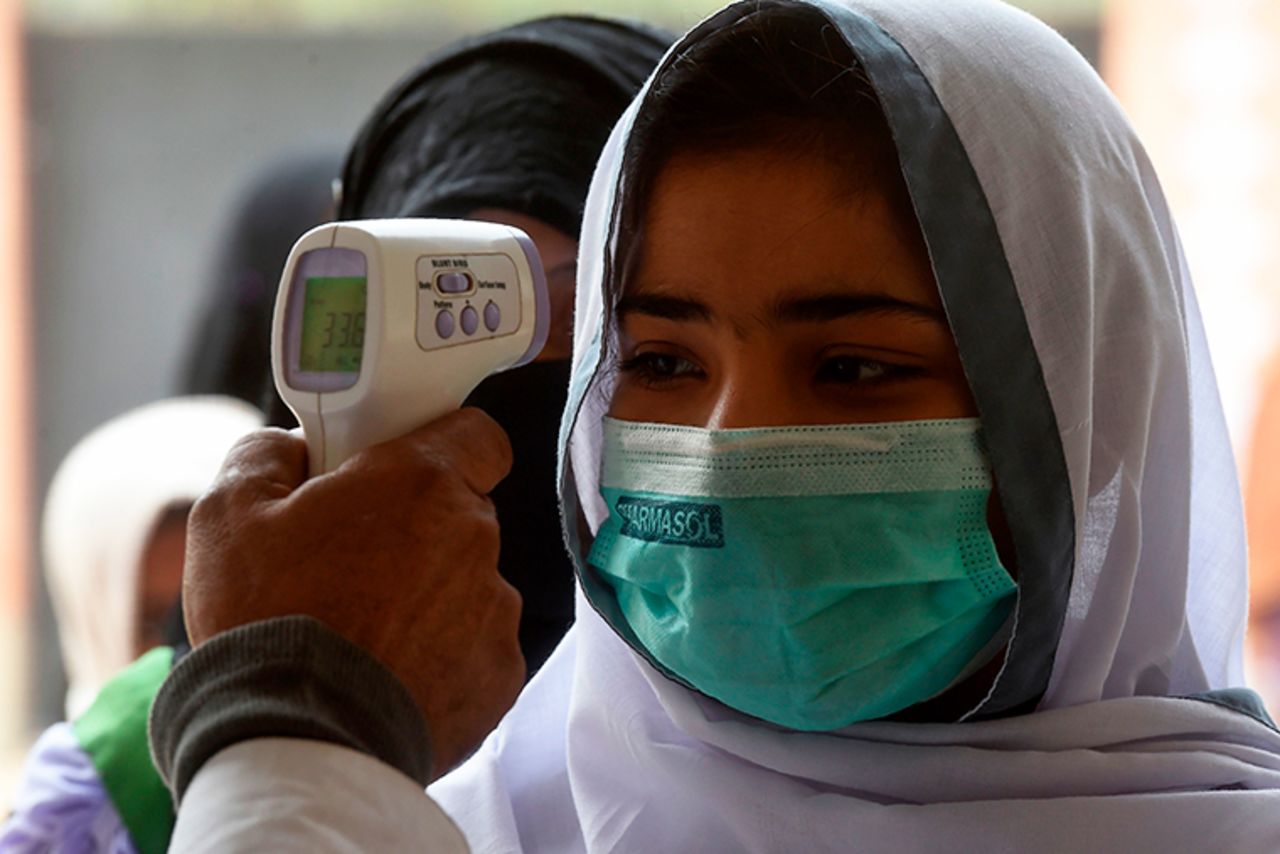 A school official checks the body temperature of students wearing face masks as they enter a school amid the coronavirus pandemic in Karachi, Pakistan, on November 25, 2020.