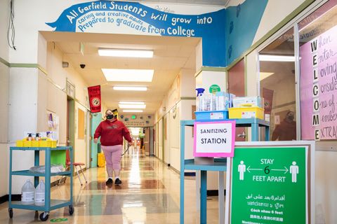 Mirna Sanchez walks down the halls stocked with a sanitizing station and social distancing markers during the first day of partial in-person instruction at Garfield Elementary School in Oakland, California, on Tuesday, March 30. Garfield Elementary School partially re-opened for students in grades kindergarten through second grade on Tuesday, March 30. 