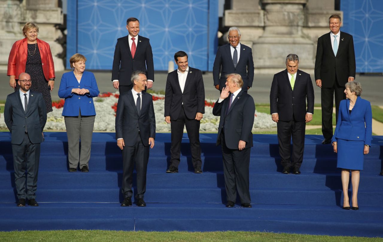 President Donald Trump holds his hand to his face as he says something to other heads of state and governments, including German Chancellor Angela Merkel, British Prime Minister Theresa May, NATO Secretary General Jens Stoltenberg and Greek Prime Minister Alexis Tsipras, gathered for a group photo at the evening reception and dinner at the 2018 NATO Summit on July 11, 2018 in Brussels, Belgium.