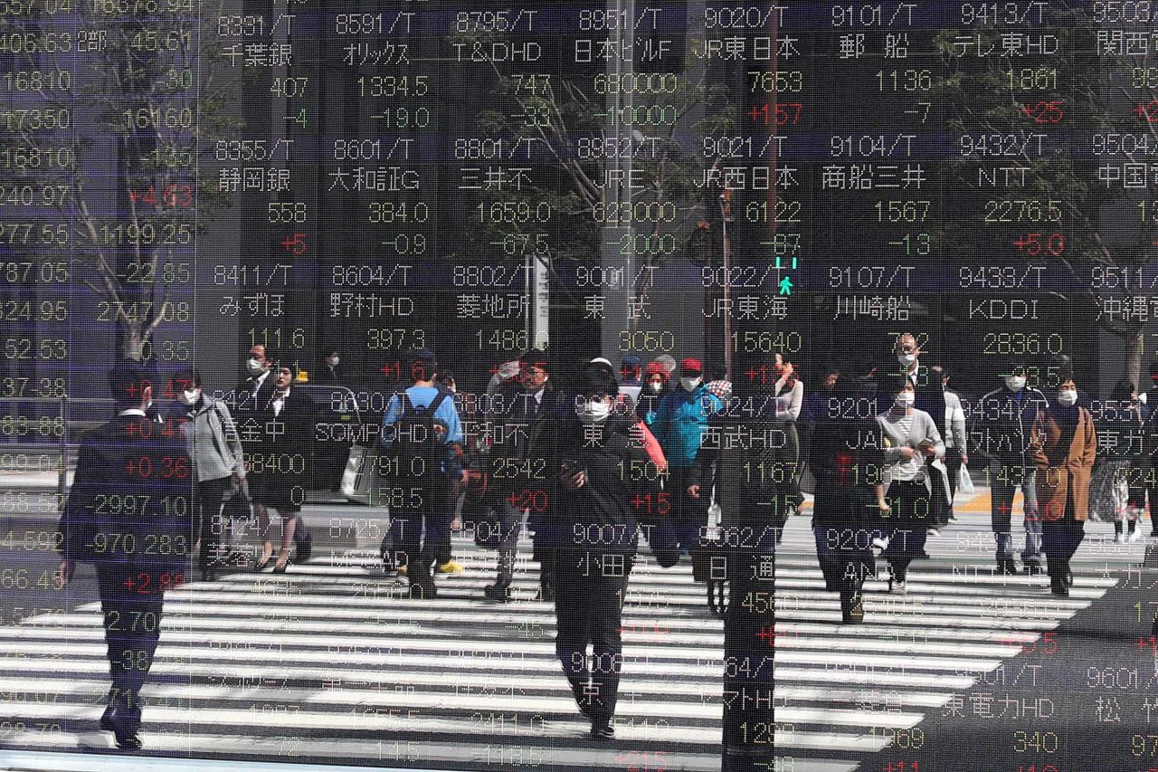 Electronic stock market displays reflect pedestrians in Tokyo, Japan, on March 16.