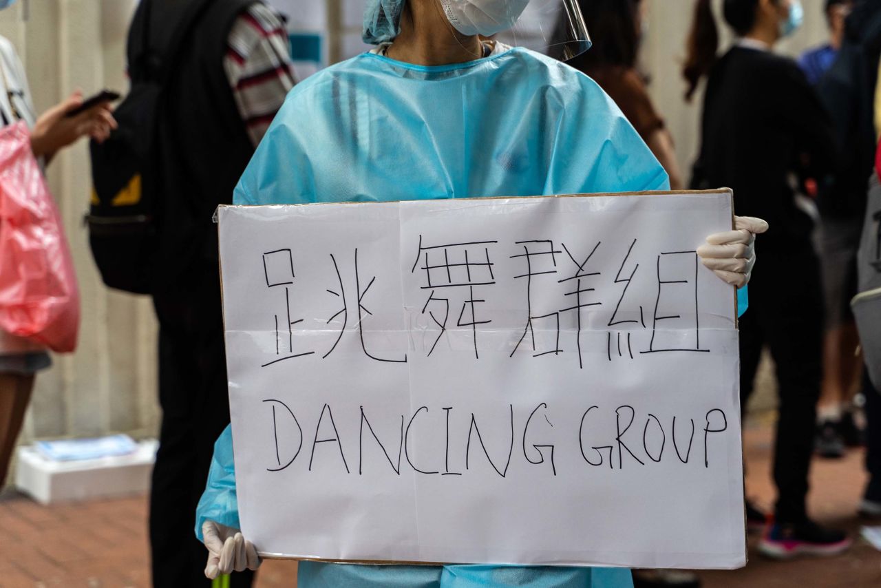 A health care worker holds a sign reading "Dancing Group," referring to the dance club coronavirus cluster, as people line up at a testing center in the Yau Ma Tei district of Hong Kong on Monday.