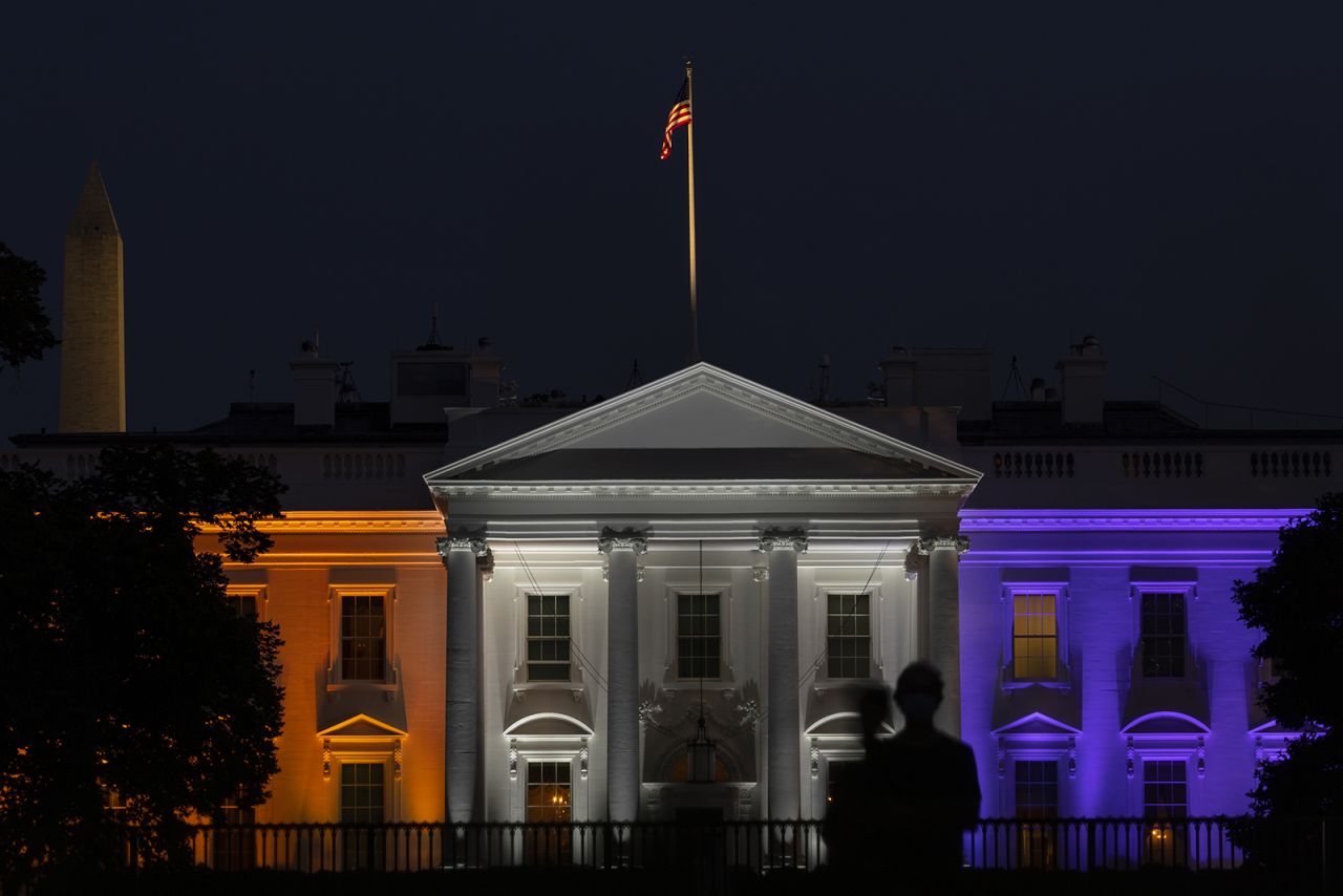 A person stands outside of the White House lit in purple and gold to mark the 100th anniversary of women's suffrage during the third night of the Republican National Convention in Washington on Wednesday, August 26. 