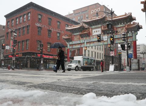 Snow falls as a pedestrian crosses the street in Chinatown in Washington, DC. 