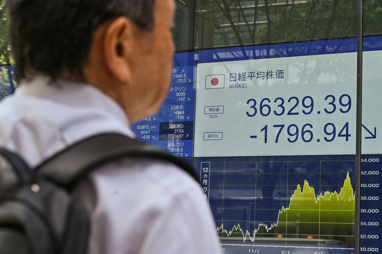 A man looks at a display board showing the morning numbers on the Tokyo Stock Exchange along a street in Tokyo on August 2.