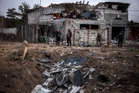 Police officers and residents stand next to a shell crater and damaged home in Kyiv, Ukraine on March 12. 