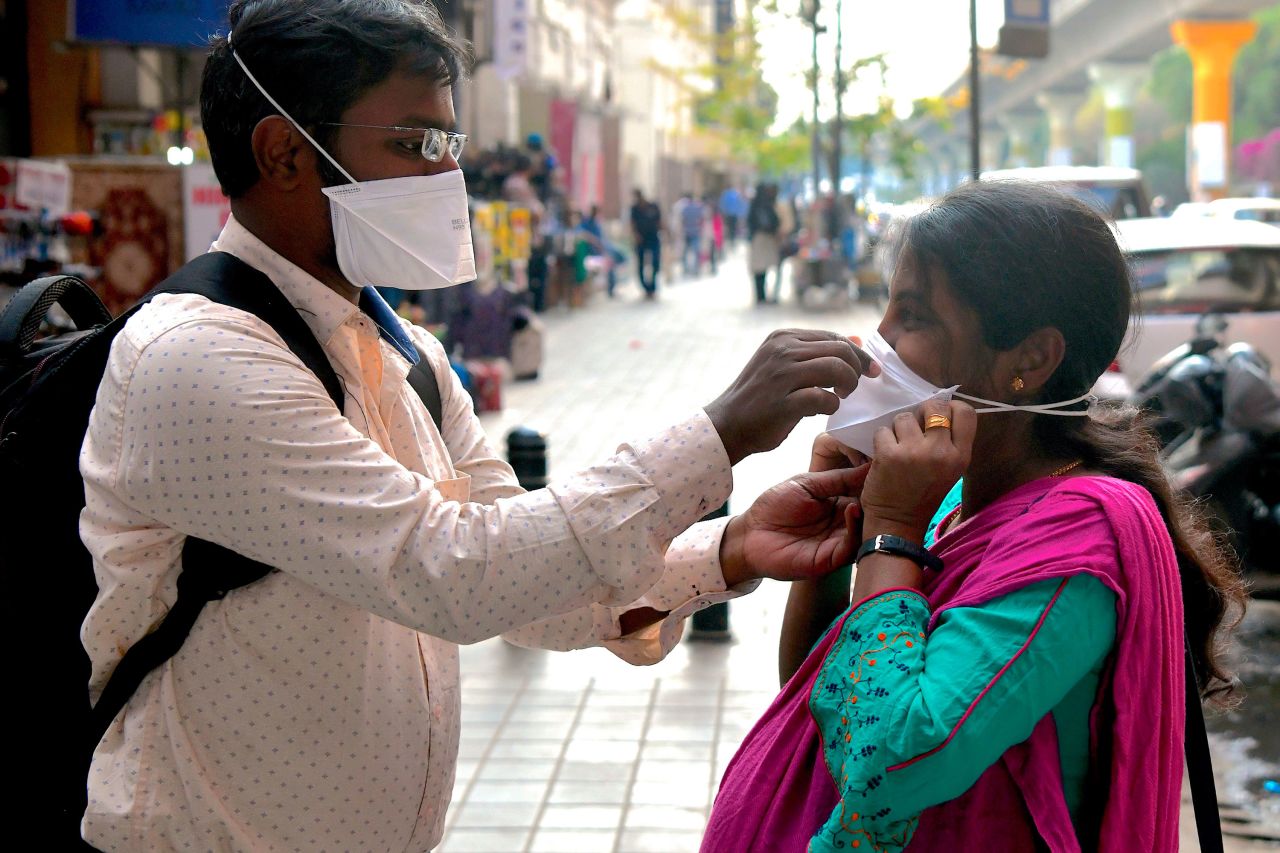 A man helps a woman put on a face mask outside of a metro station in Bangalore, India on March 5.