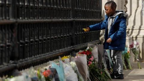 A young boy places flowers on the gate at Buckingham Palace in London.