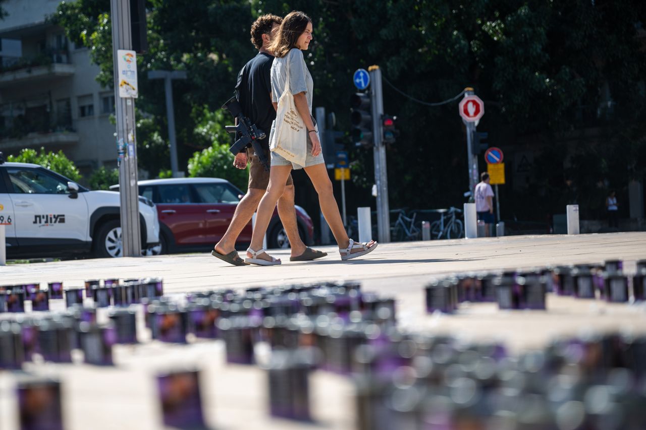 A man walks with a gun while holding a woman's hand near memorial candles laid next to the “We Stand With Israel” memorial display in Tel Aviv, Israel, on October 20.