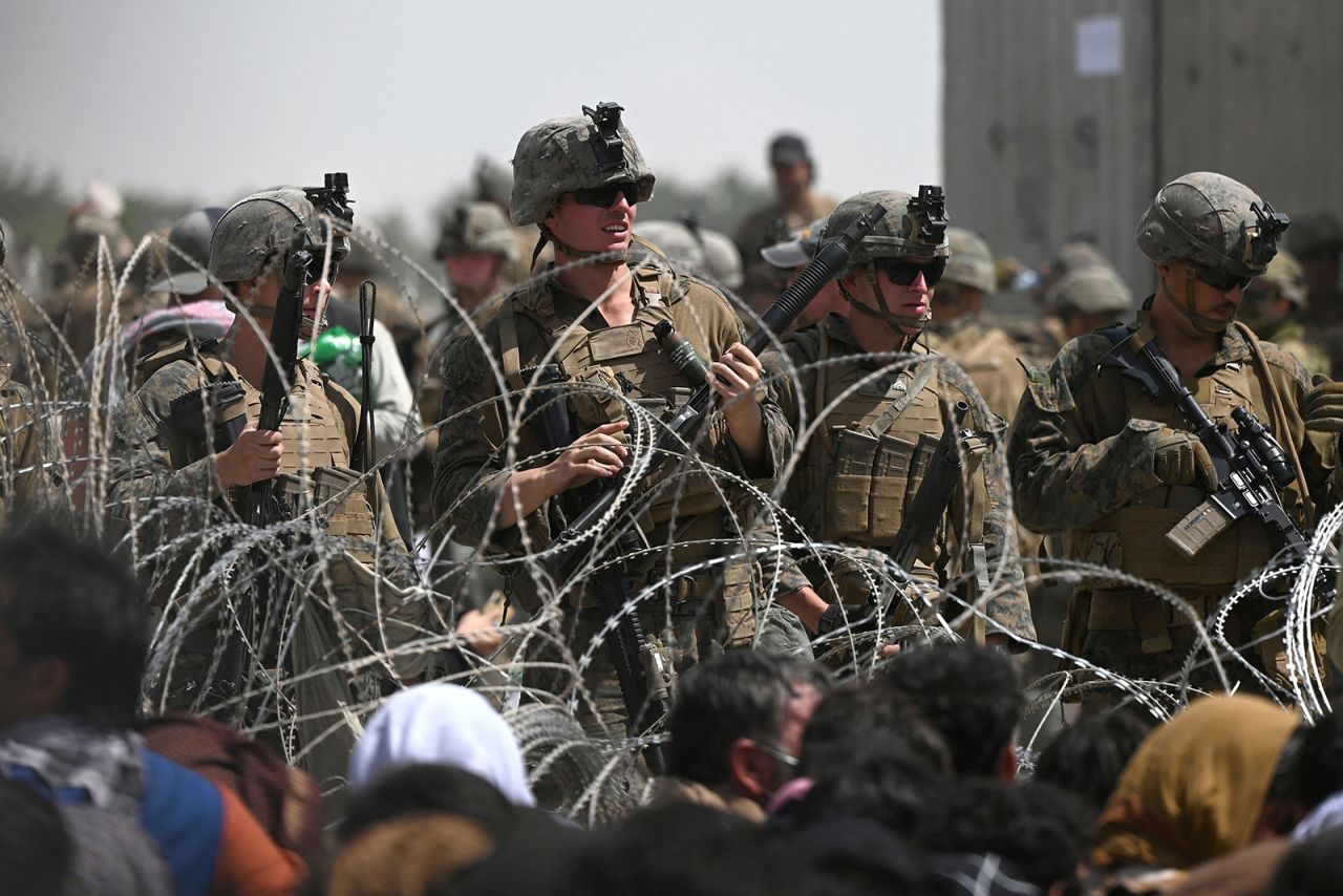 US soldiers stand guard behind barbed wire as Afghans sit on a roadside near the military part of the airport in Kabul on August 20.