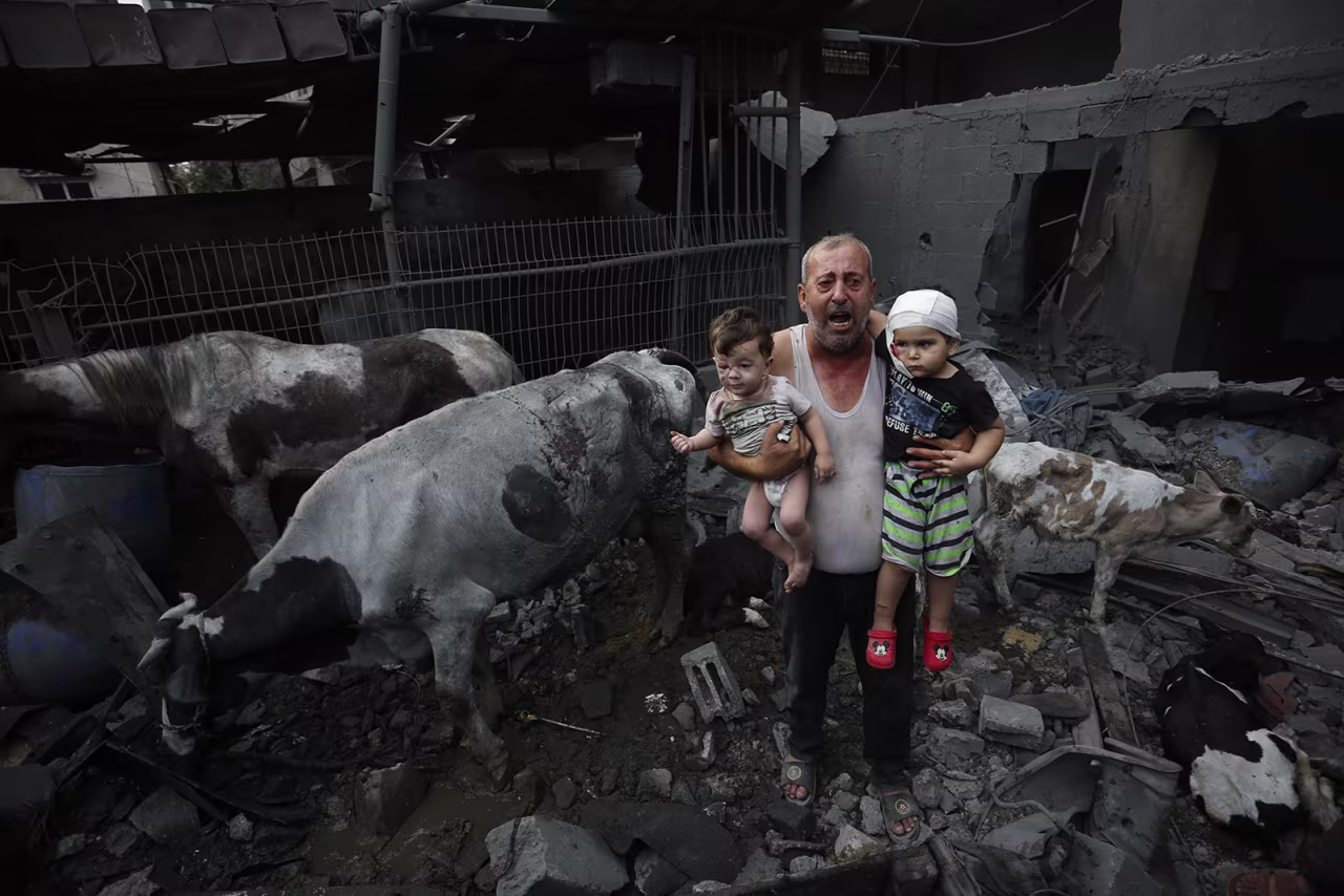 A man holds wounded children near livestock around heavily damaged buildings after Israeli attacks at Nuseirat Refugee Camp in Gaza City on Sunday, October 29. 