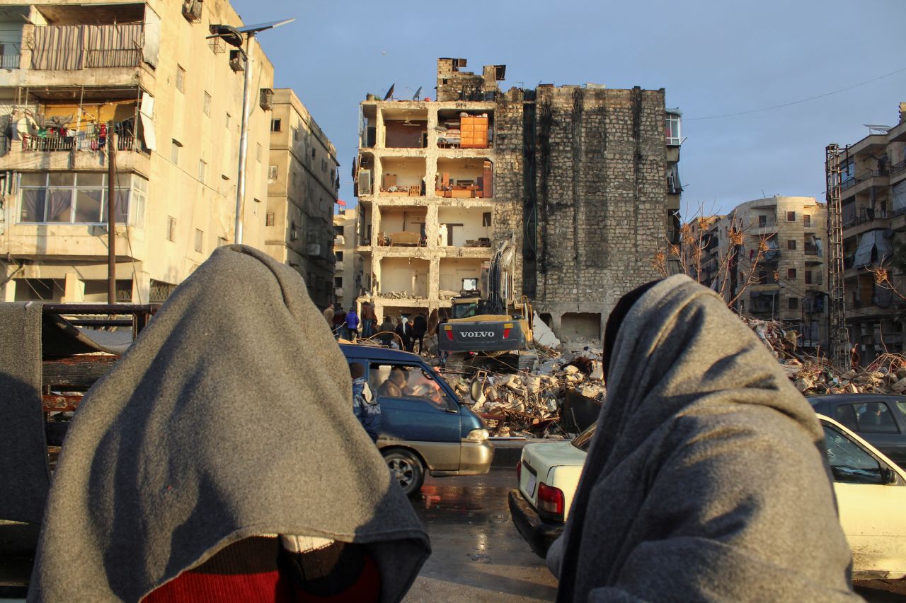 People wrapped in blankets look at the rubble as the search for survivors continues in Aleppo, Syria on Tuesday.