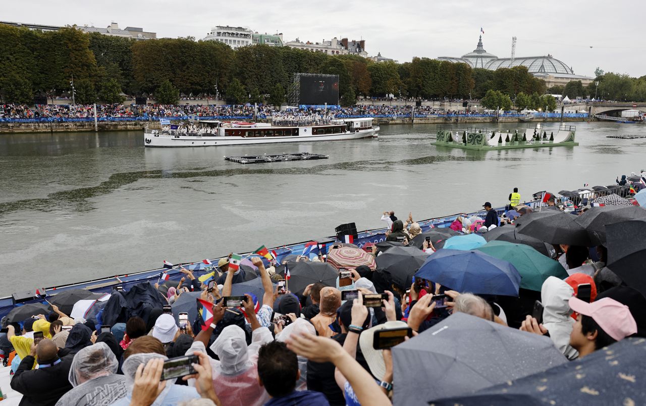 Spectators in stands on the bank of the river Seine are seen as the delegation of Greece passes in the floating parade during the Opening Ceremony of the Olympic Games.