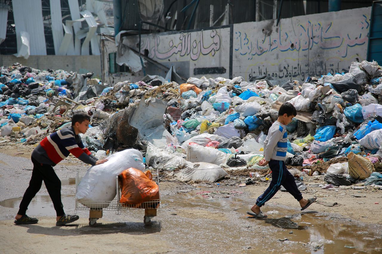 A child walks past a pile of household refuse as he transports objects, in a street in Gaza on March 28.