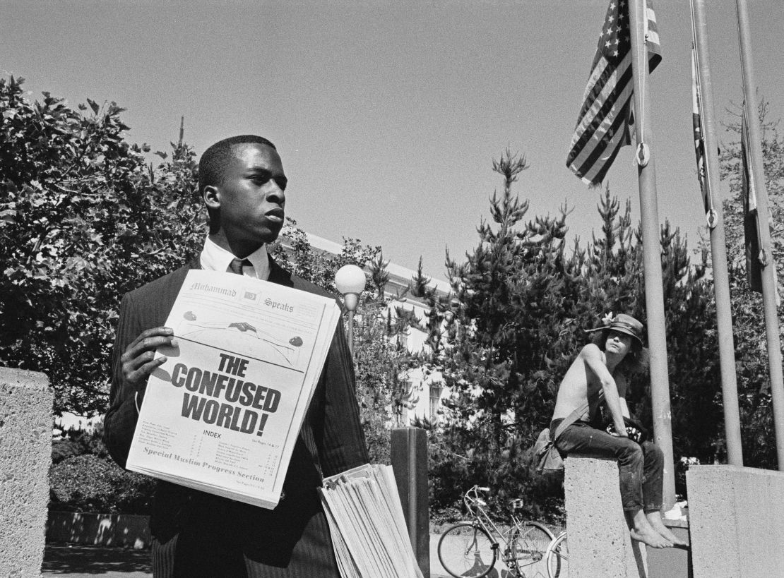 An untitled, undated photograph of a Black man holding a copy of "Muhammad Speaks," the official newspaper of the Nation of Islam. The image, taken by South African photographer Ernest Cole, is one of thousands taken during his time in exile in the United States.