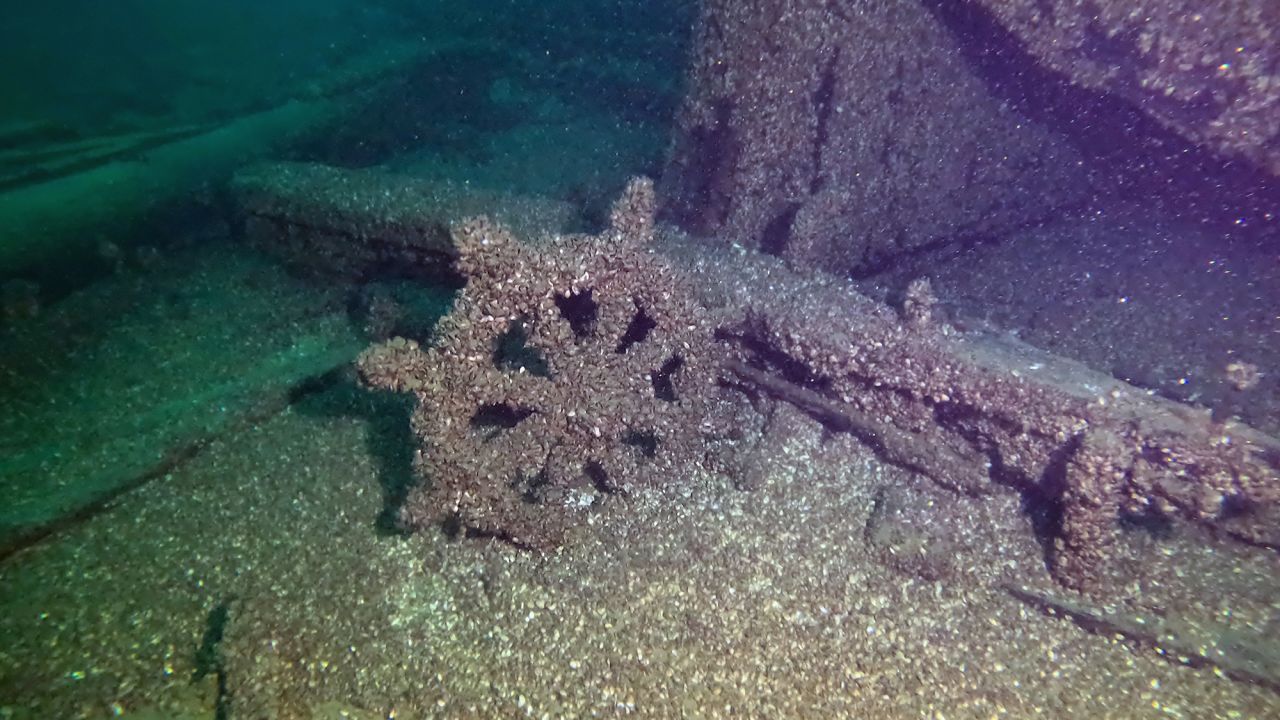 The ship's wheel sits on the lake bottom just off the King's stern. The top of the King's stern, including the pilot house below apart as a massive rush of air was forced backward when her iron ore cargo slid forward as she sank.

