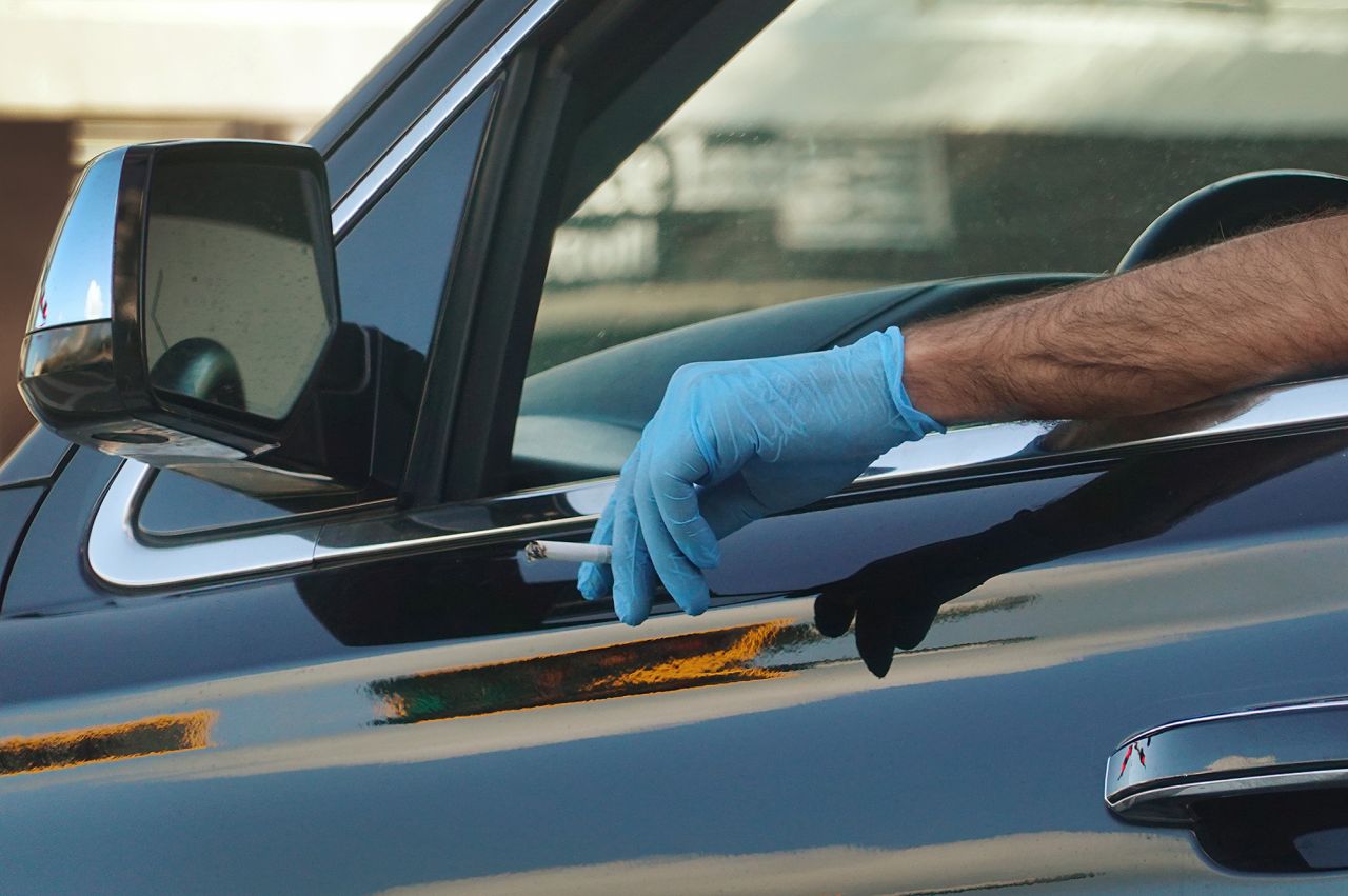 A person holds a cigarette out a car window while wearing a protective glove as large numbers of people take measures to protect themselves from the coronavirus pandemic on March 24, 2020 in Miami.