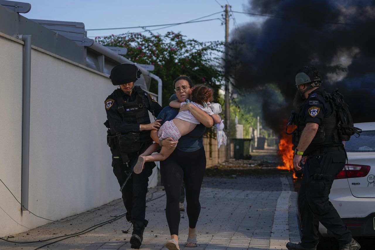 Israeli police officers evacuate a woman and a child from a site hit by a rocket fired from Gaza, in Ashkelon, southern Israel, on October 7.