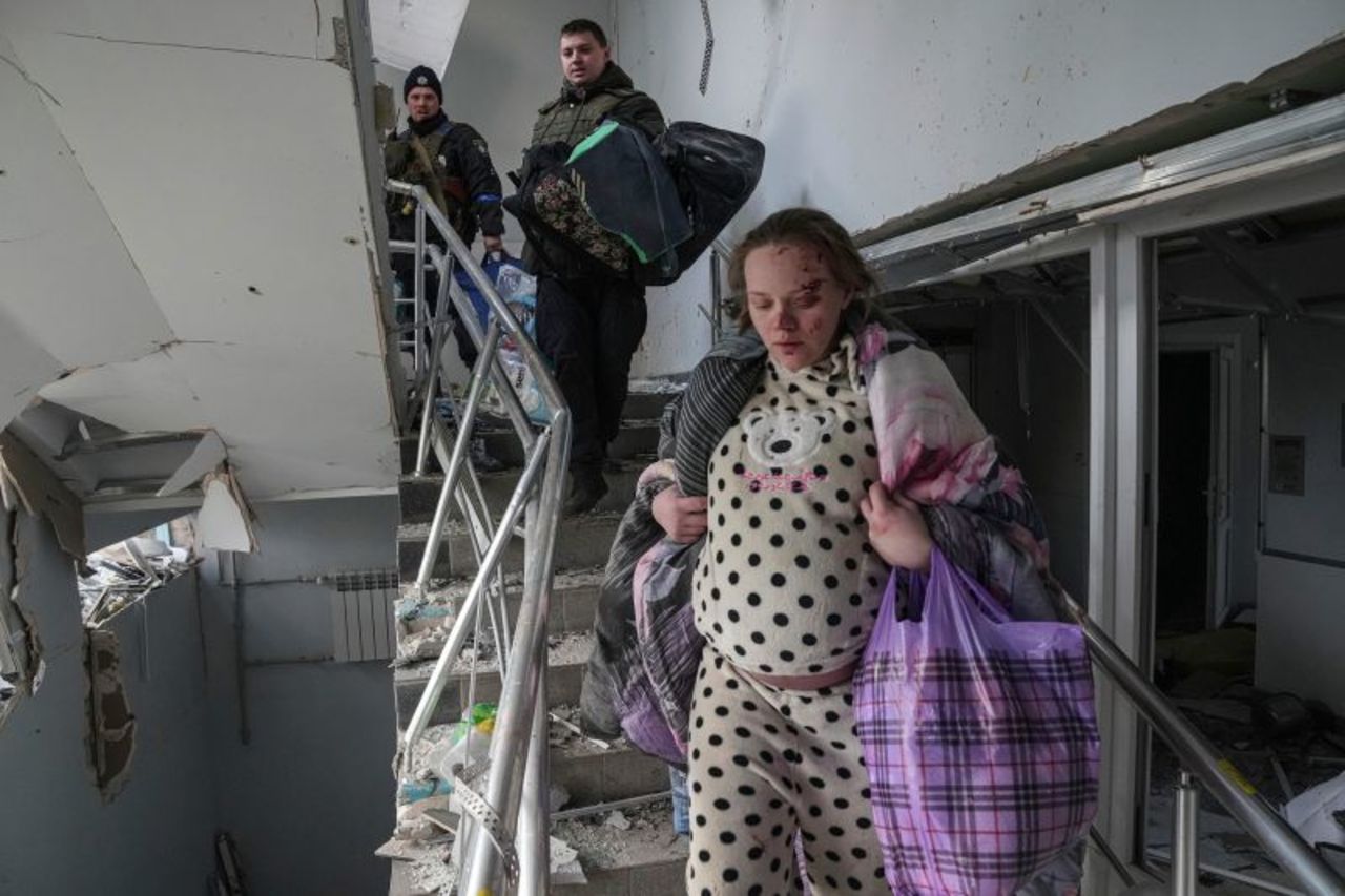 An injured pregnant woman leaves the damaged hospital with her belongings.