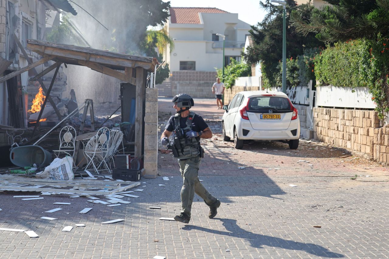 A member of the Israeli forces runs past a fire rages in a house in Ashkelon, following a rocket attack from the Gaza Strip on southern Israel on October 7, 2023.