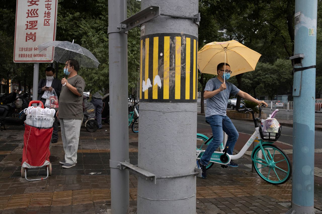 A man wearing a face mask to curb the spread of the coronavirus takes the opportunity to sell umbrellas as it rains in Beijing on Thursday, June 18, 2020. 