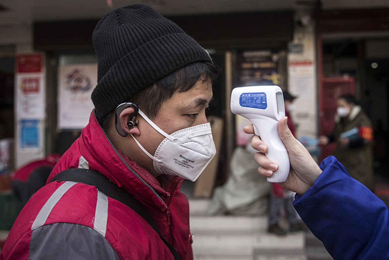 A community worker checks the temperature of courier in an Express station on Wednesday, January 29, in Wuhan, China.