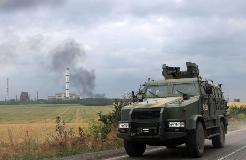 A Ukrainian armored personnel carrier (APC) rides on the road while smoke rises over the oil refinery outside the town of Lysychansk, Ukraine, on June 23.