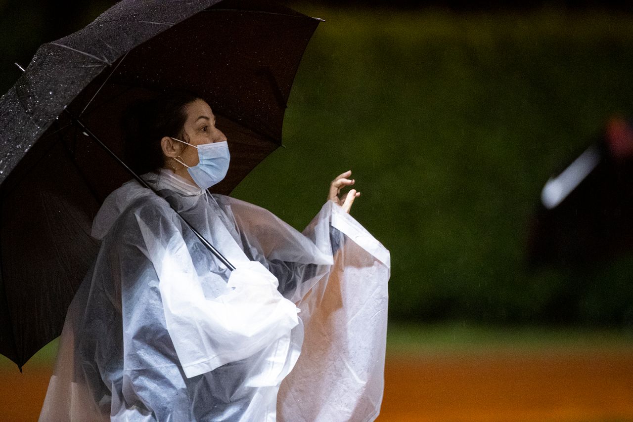 A fan wearing a mask watches the action from under an umbrella as Lipscomb Academy plays football against Brentwood Academy on Friday, August 21 in Brentwood, Tennessee. 