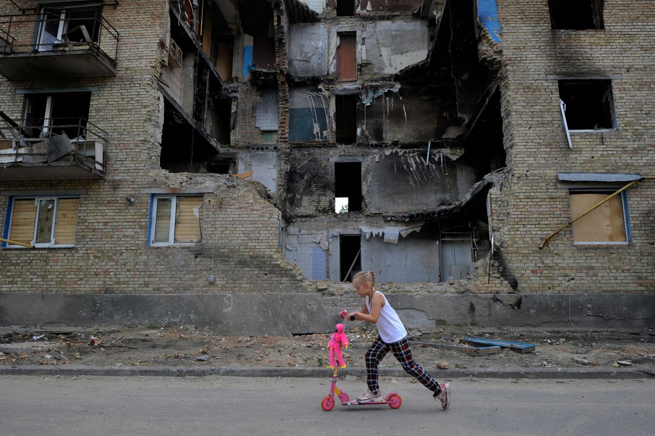 A girl rides a kick scooter past a destroyed residential building in the village of Horenka, Ukraine, on June 4.