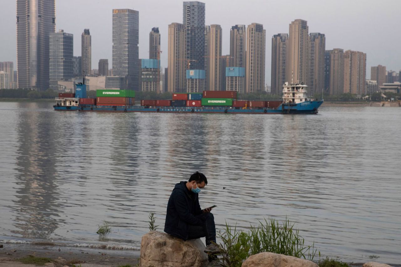 A man wearing a face mask checks his phone as a container ship cruises along the Yangtze River in Wuhan in China's central Hubei province on April 13.